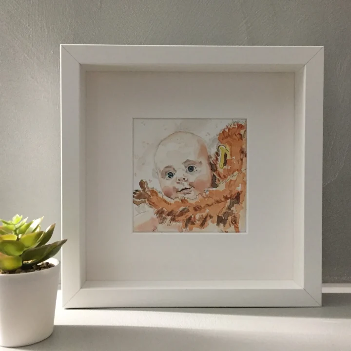 Babyportret in aquarel: het gezicht van een baby tussen oranje vormen, ingelijst in een witte lijst.
