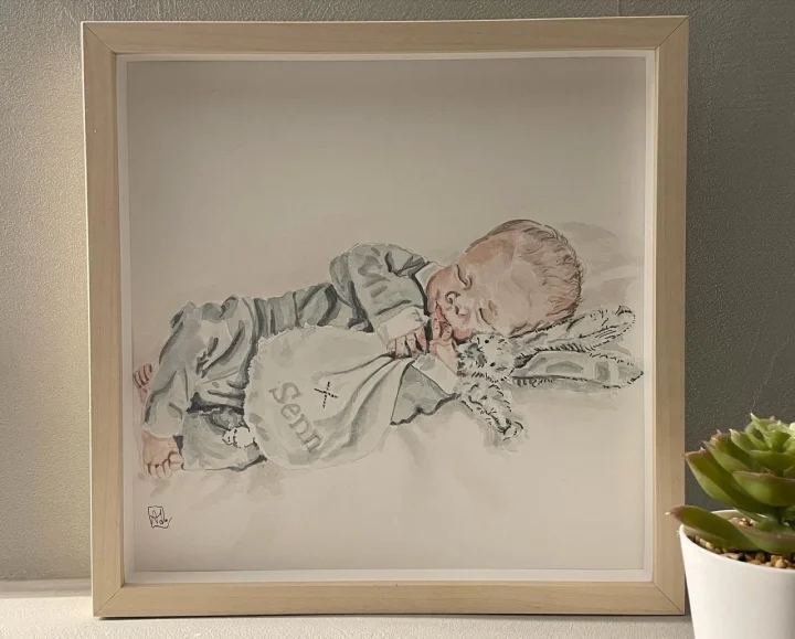 Babyportret in aquarel: een slapende baby op de zij, met fijne lijnen getekend, in een blank houten lijst.