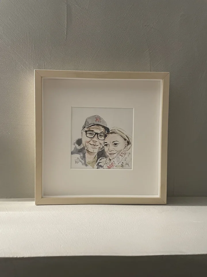 Portret in aquarel van twee mensen naast elkaar, klein ingelijst met passe-partout in een blank houten lijst.