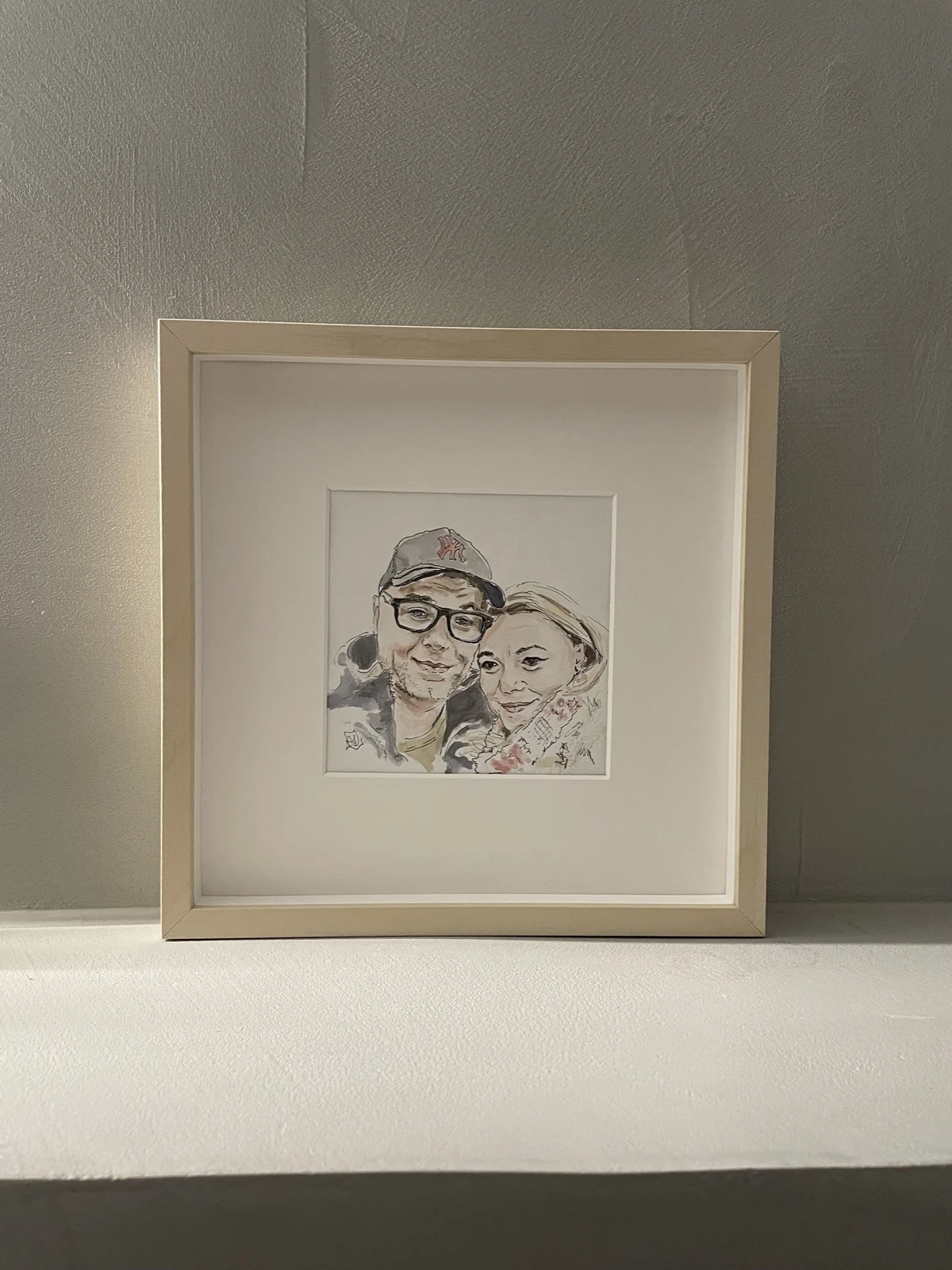 Portret in aquarel van twee mensen naast elkaar, klein ingelijst met passe-partout in een blank houten lijst.